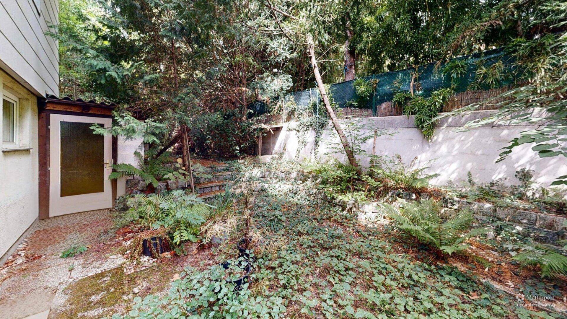 Gestufter Gartenbereich mit üppiger Bepflanzung, Treppen und einem kleinen Schuppen, naturnah gestaltet.