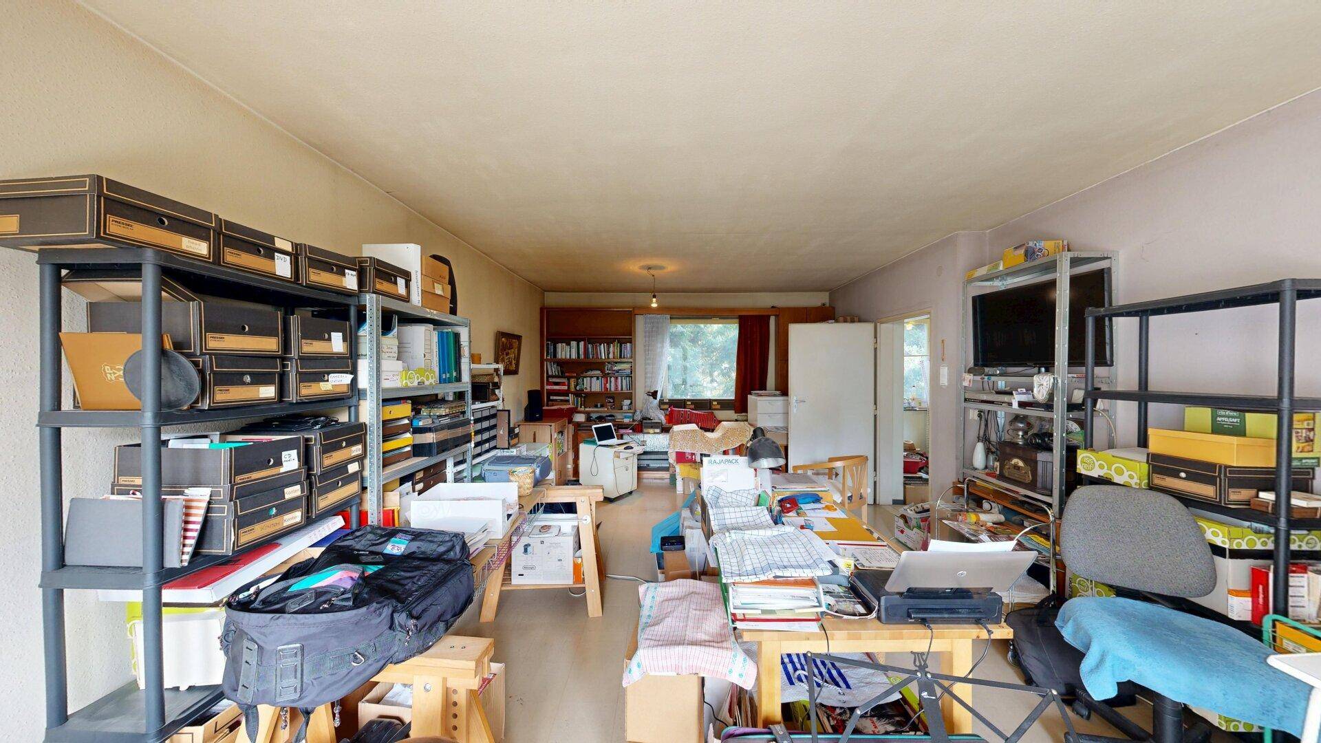 Großer, vielseitig genutzter Raum mit Regalen, Schreibtischen und Stauraum, ideal als Arbeits- oder Hobbyzimmer.