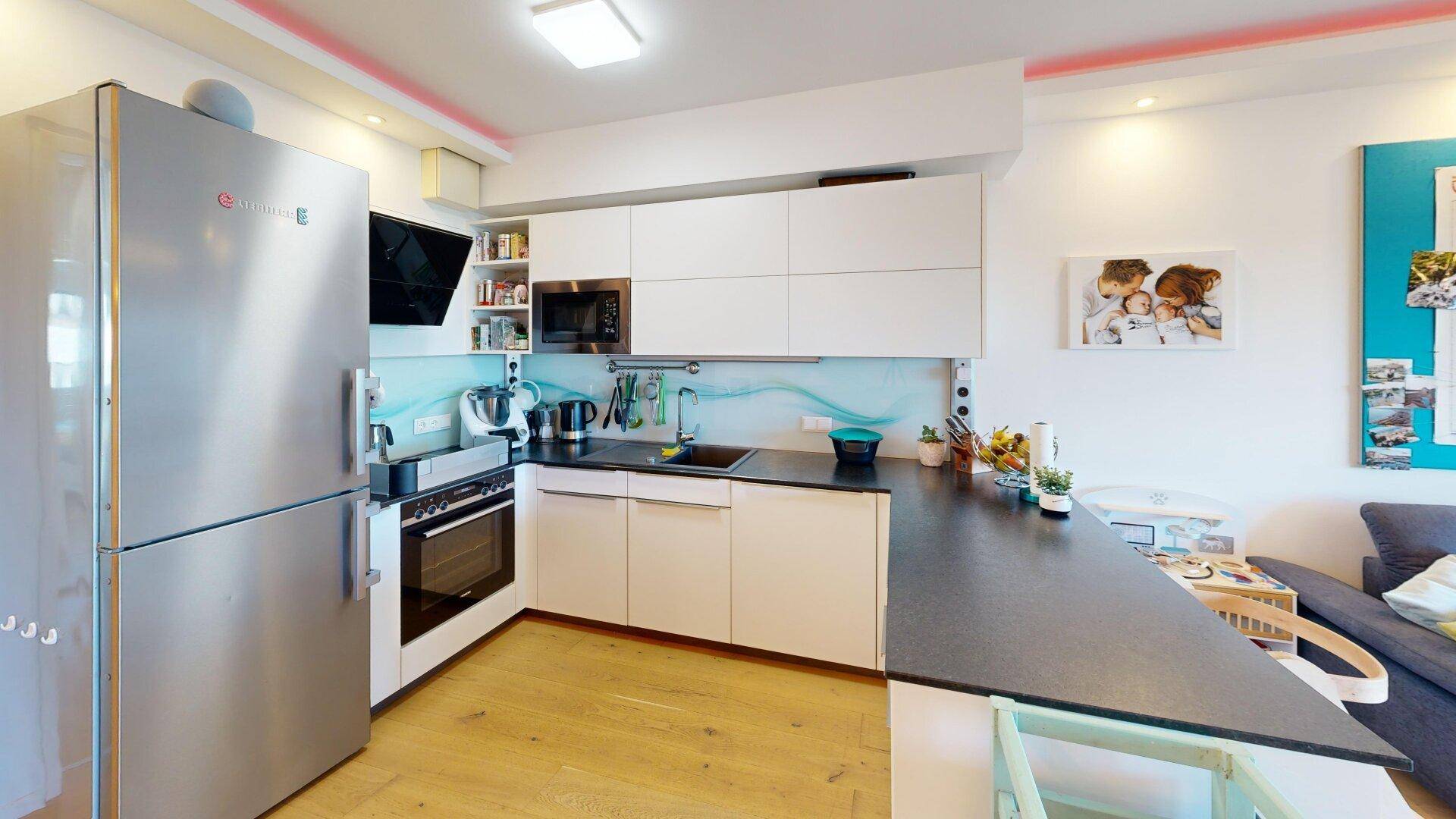 Moderne Küche mit weißen Hochglanzschränken, dunkler Arbeitsplatte und integrierten Geräten.
