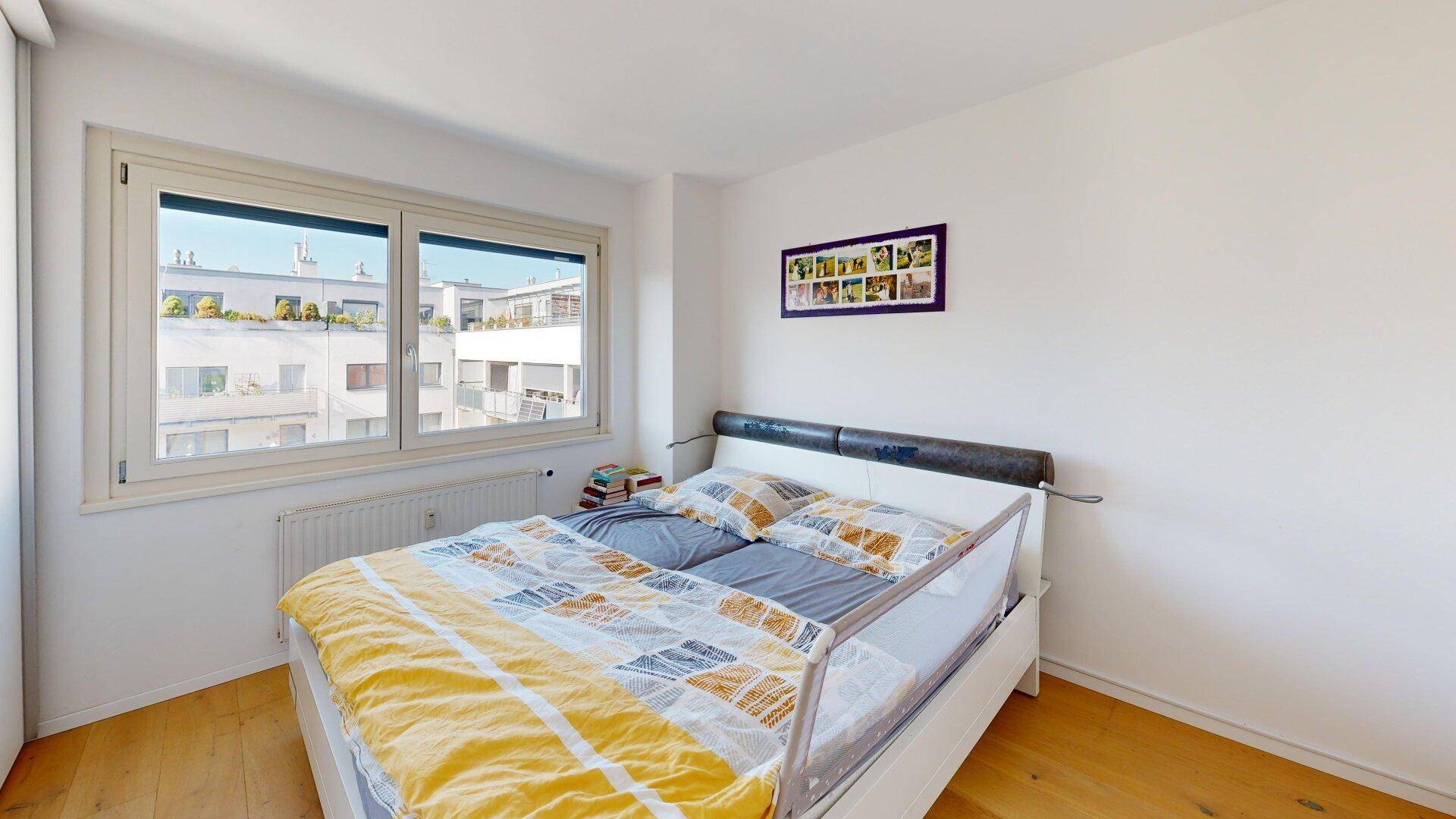 Helles Schlafzimmer mit großem Fenster, Doppelbett und Holzboden, schlicht und einladend.