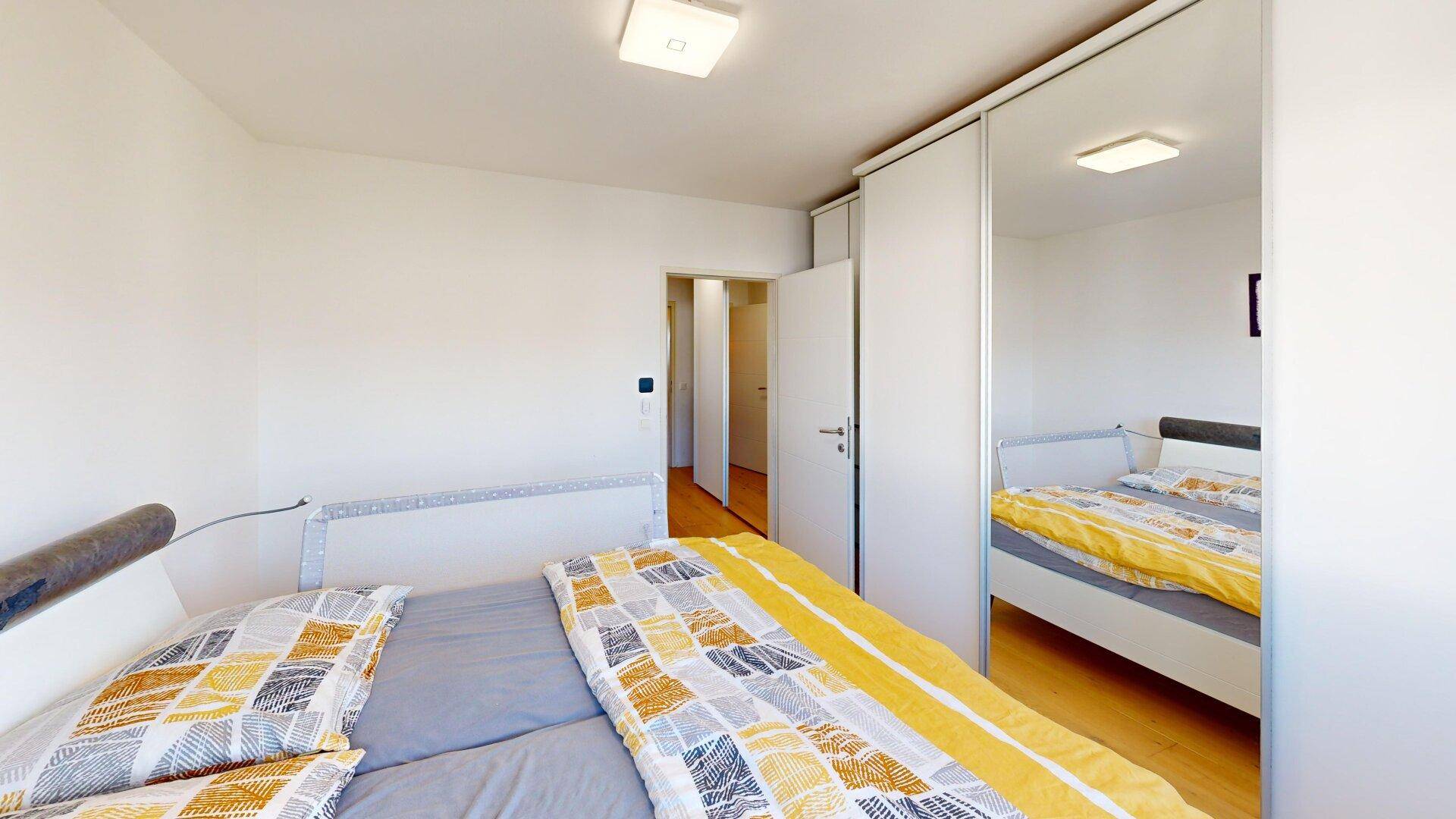 Helles Schlafzimmer mit Doppelbett, Spiegelschrank und Holzboden, modern und funktional eingerichtet.