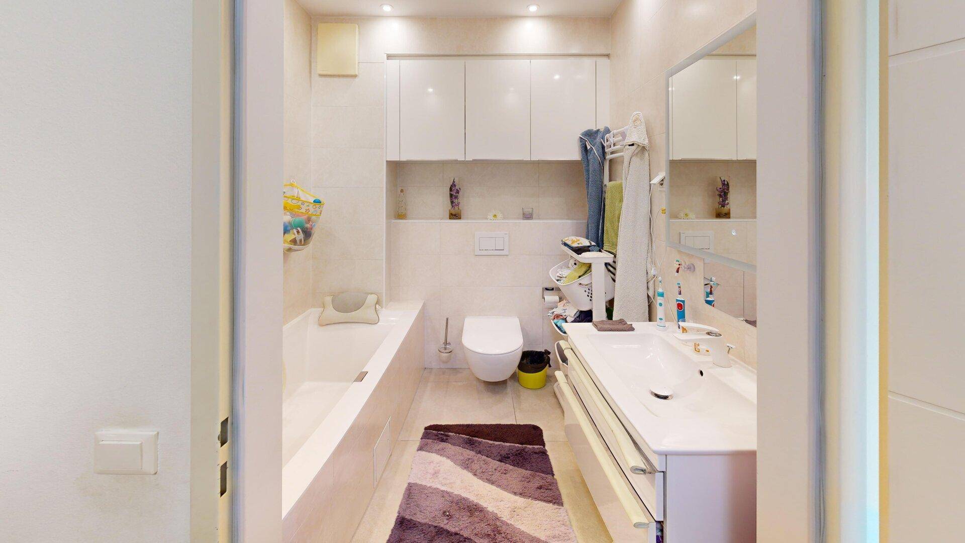 Geräumiges Badezimmer mit Badewanne, Doppelwaschbecken und hellen Fliesen, elegant und funktional.