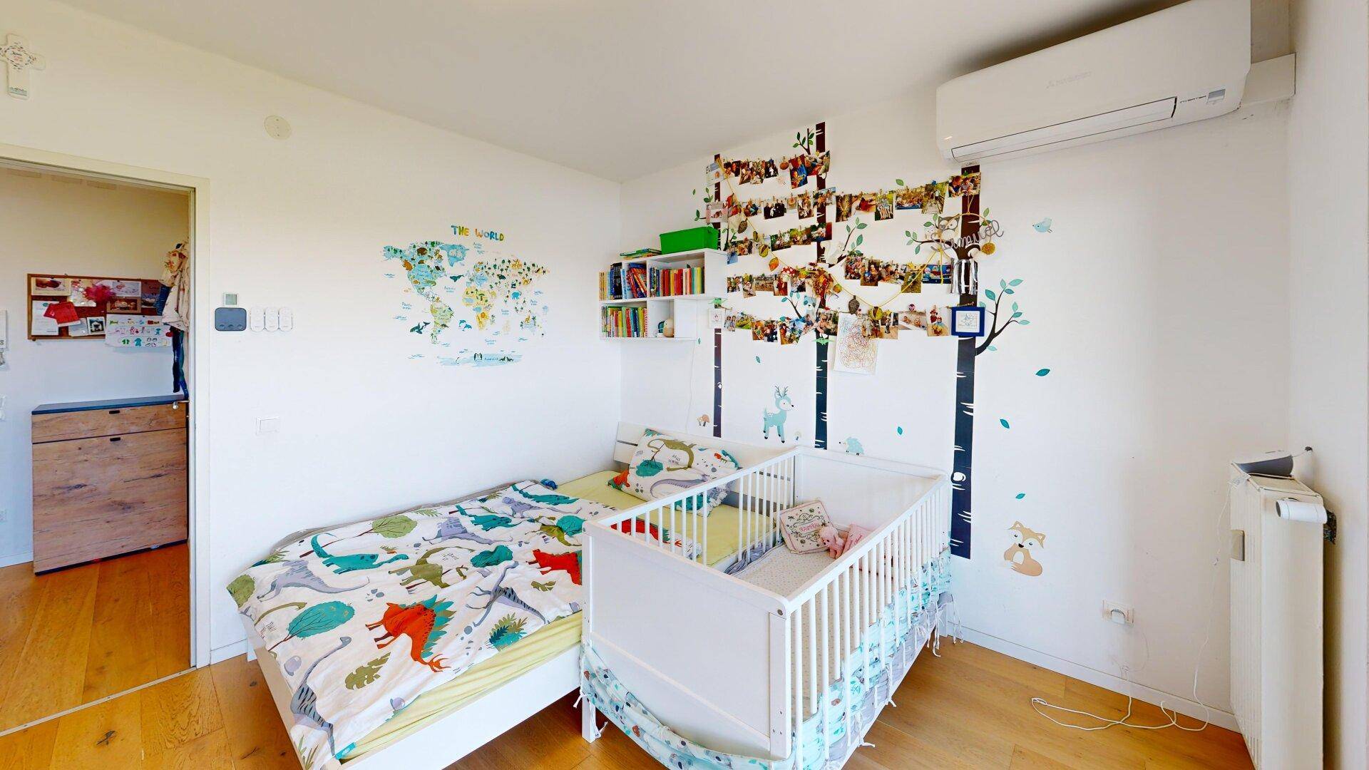 Helles Kinderzimmer mit Einzelbett, Babybett und spielerischer Wanddekoration, freundlich gestaltet.