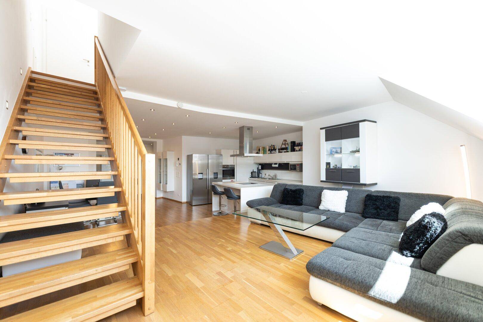 Heller Wohnbereich mit Holztreppe, großem Sofa und offener Gestaltung zum Essbereich und zur Küche.