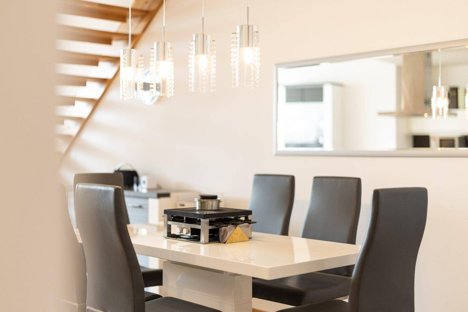 Detailaufnahme des eleganten Esstisches mit modernen Hängelampen und Spiegel an der Wand.