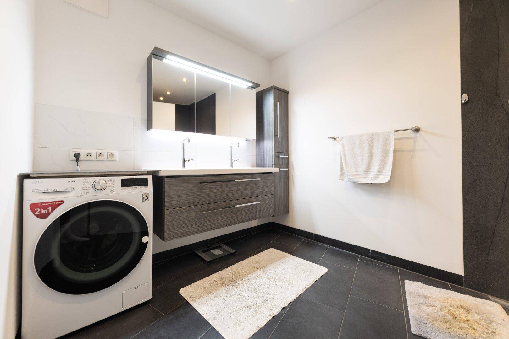 Geräumiges Badezimmer mit Doppelwaschbecken, Spiegelschrank und integrierter Waschmaschine.