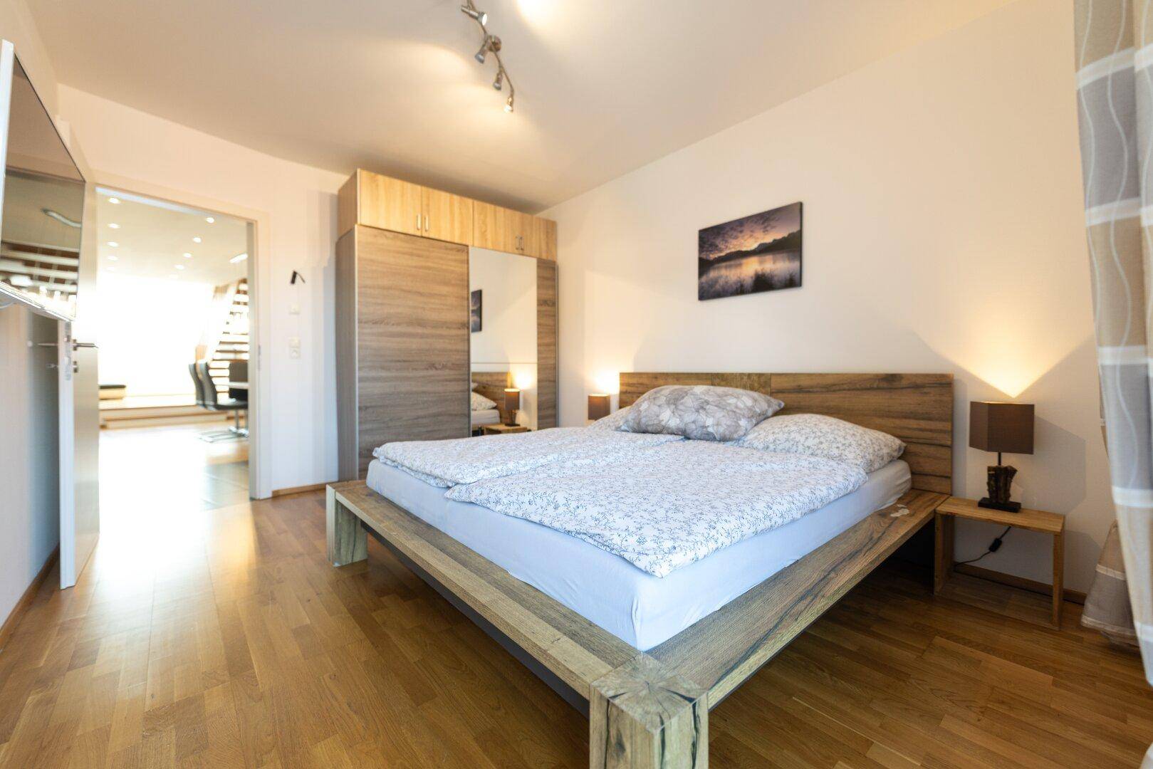 Gemütliches Schlafzimmer mit Holzbett, Parkettboden und großem Kleiderschrank, offen zum Wohnbereich.