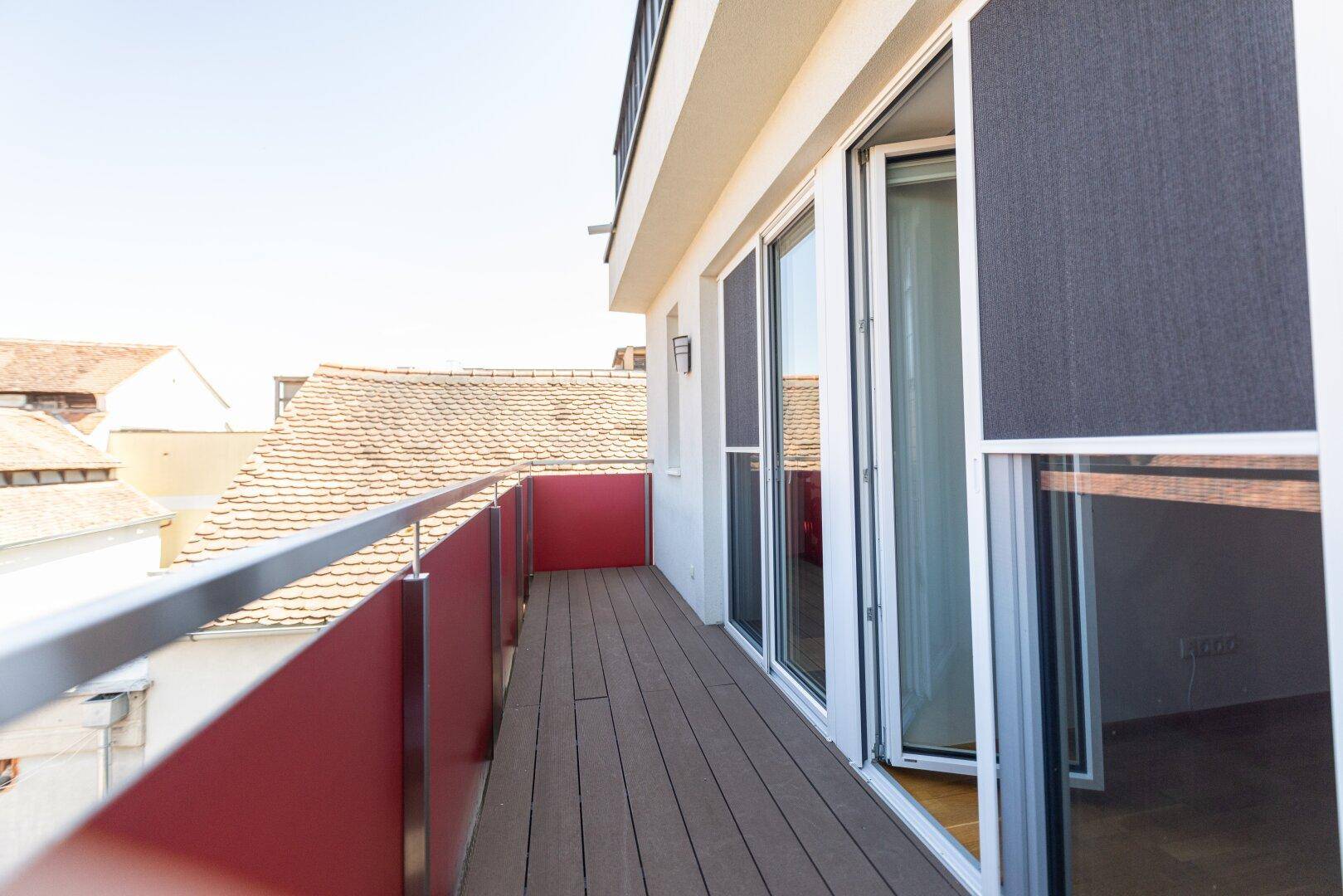 Langer, schmaler Balkon mit modernem Geländer und Blick auf die umliegenden Dächer.