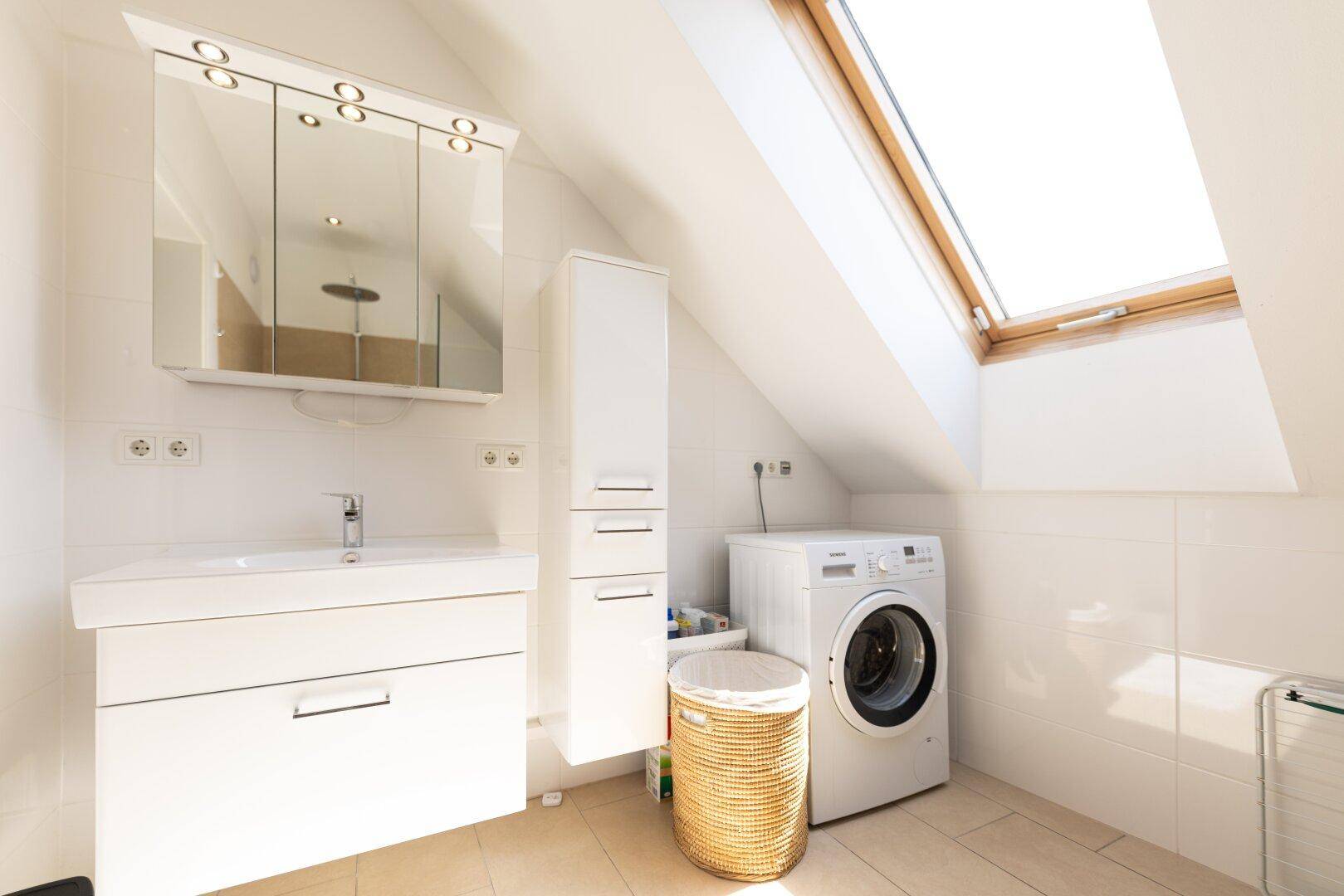 Helles Badezimmer im Dachgeschoss mit Dachfenster, Waschtisch und Waschmaschine.