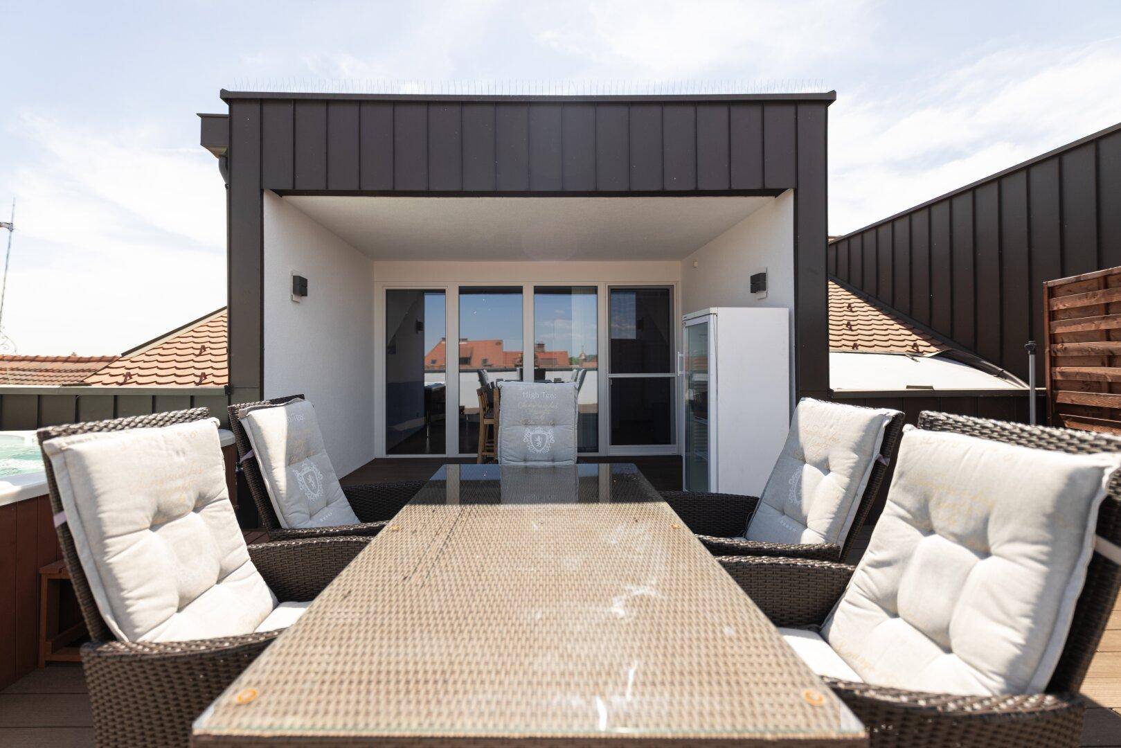 Überdachter Außenbereich auf der Dachterrasse mit Esstisch und Blick auf die Umgebung.