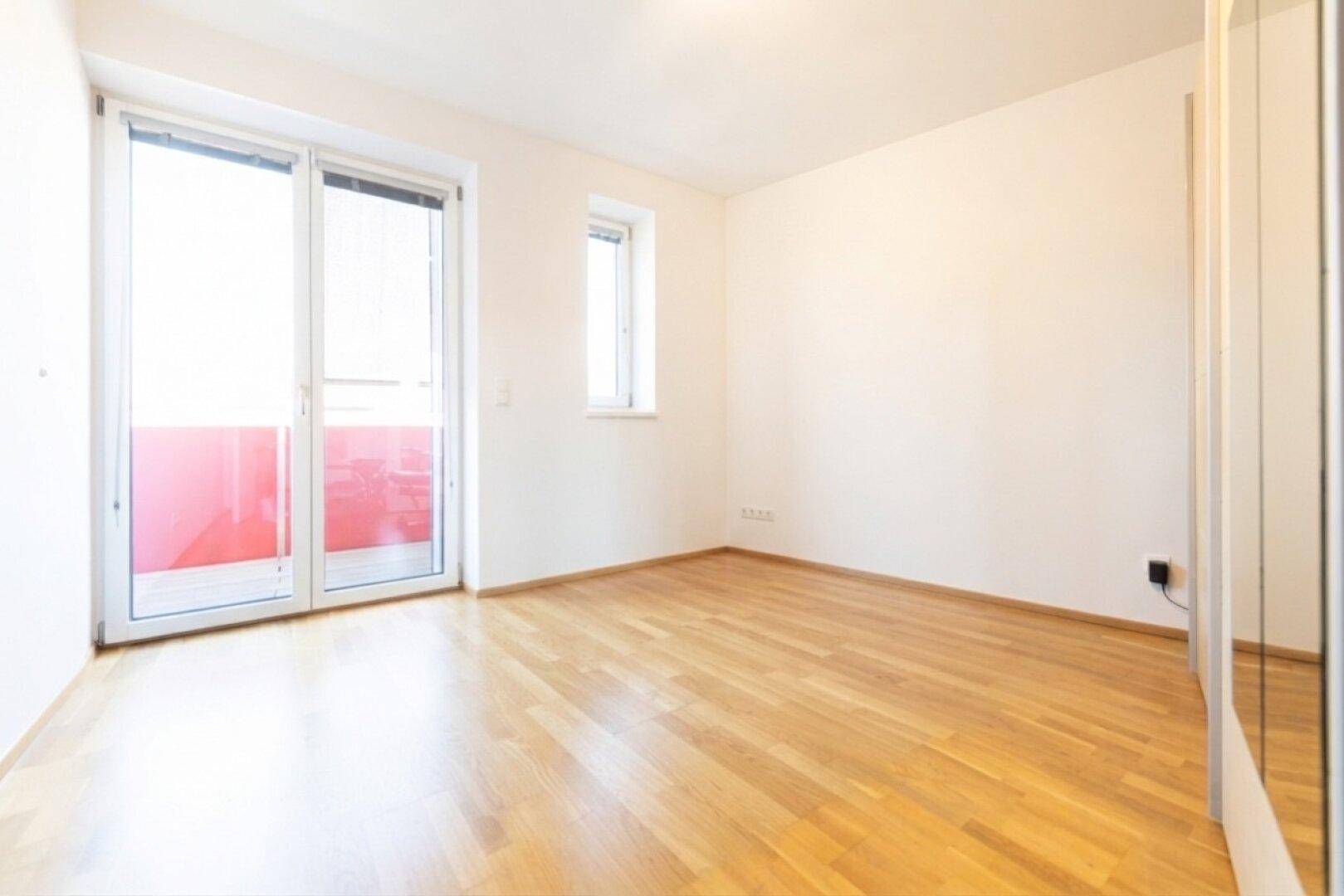 Leeres Schlafzimmer mit Parkettboden und Zugang zu einem Balkon, ideal für individuelle Gestaltung.