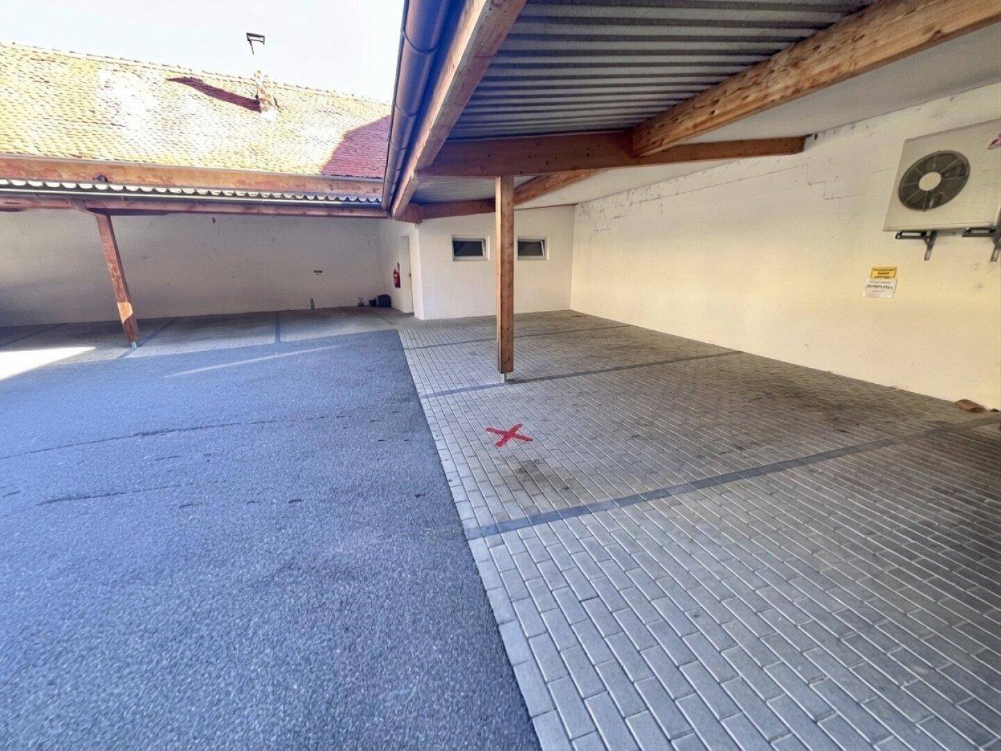Überdachter Stellplatz mit Holzbalkenkonstruktion und gepflastertem Boden für Fahrzeuge.