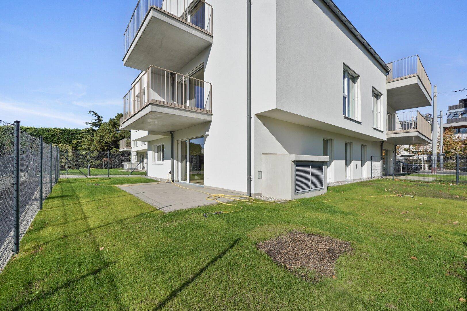 Moderne Gebäudefassade mit mehreren Balkonen und einem gepflegten Rasenbereich im Erdgeschoss.