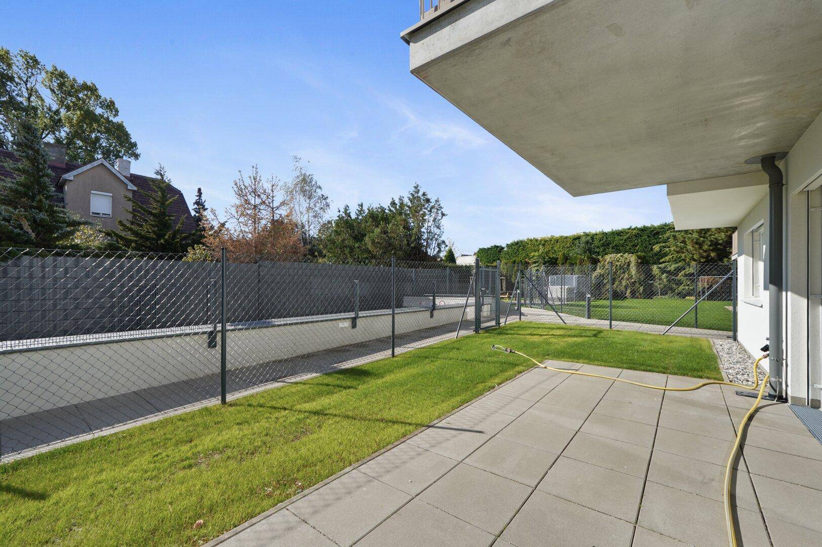 Gepflasterte Terrasse mit angrenzendem Rasen und einem stabilen Zaun, ideal für Entspannung im Freien.