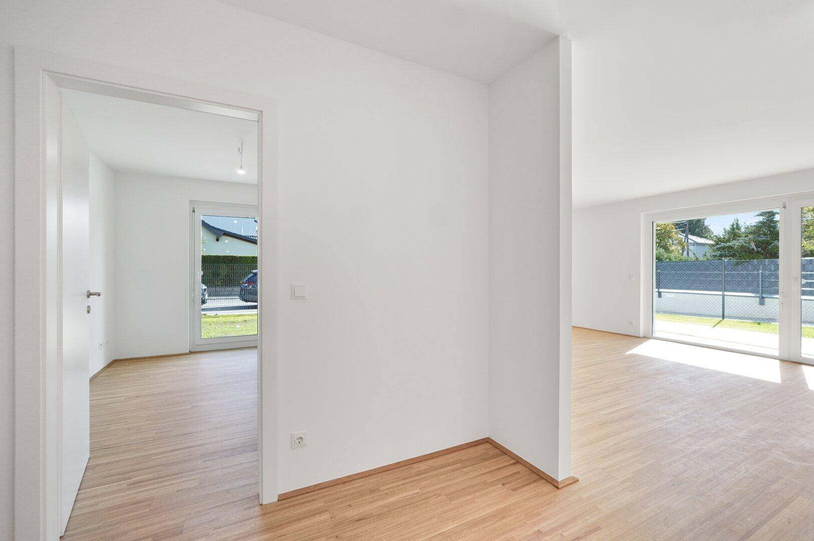 Heller Innenraum mit Holzfußboden und Blick durch eine Tür in einen weiteren Raum und nach draußen.