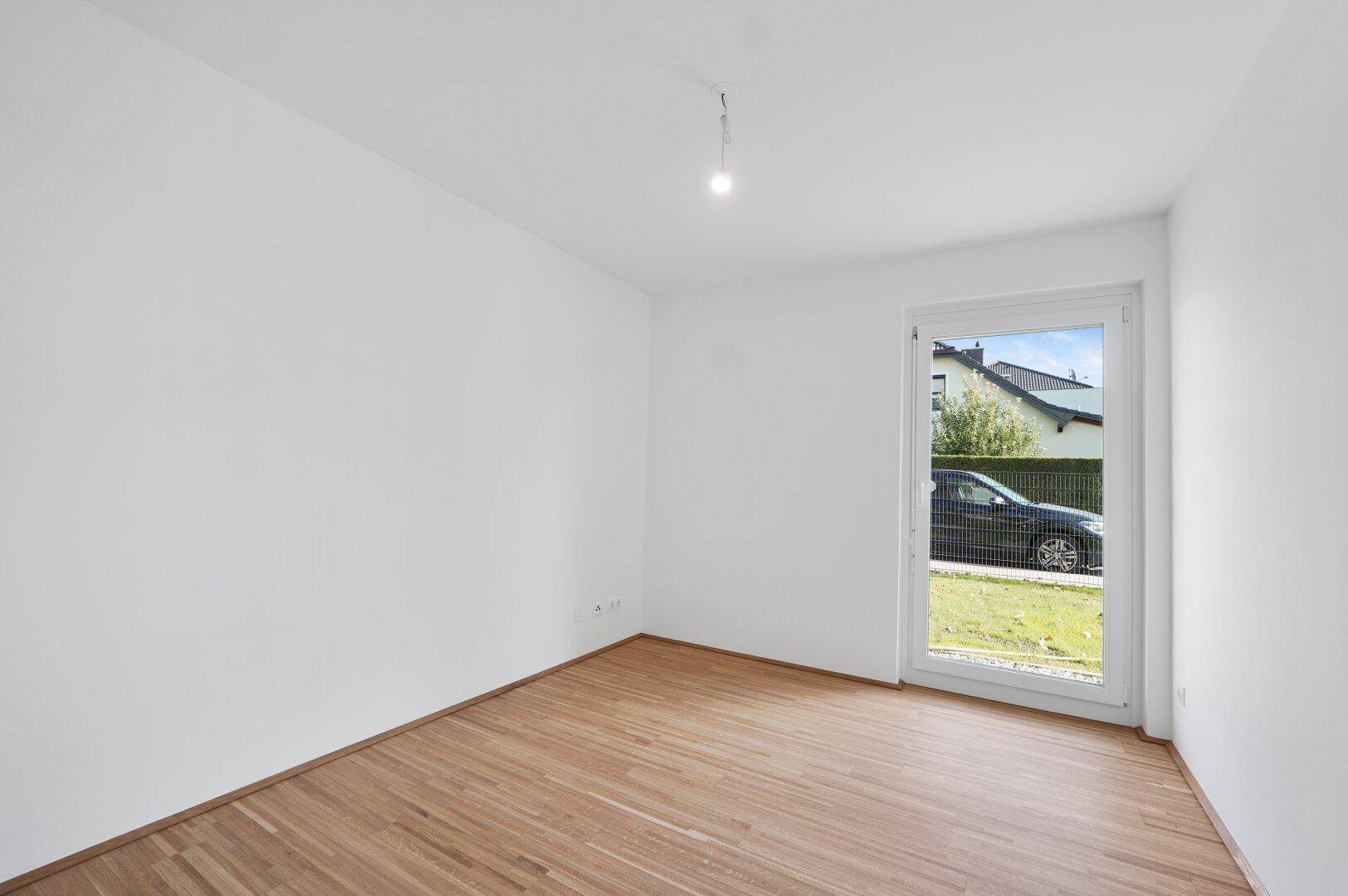 Leeres Zimmer mit Holzfußboden und einer Tür, die den Zugang zum Außenbereich ermöglicht.