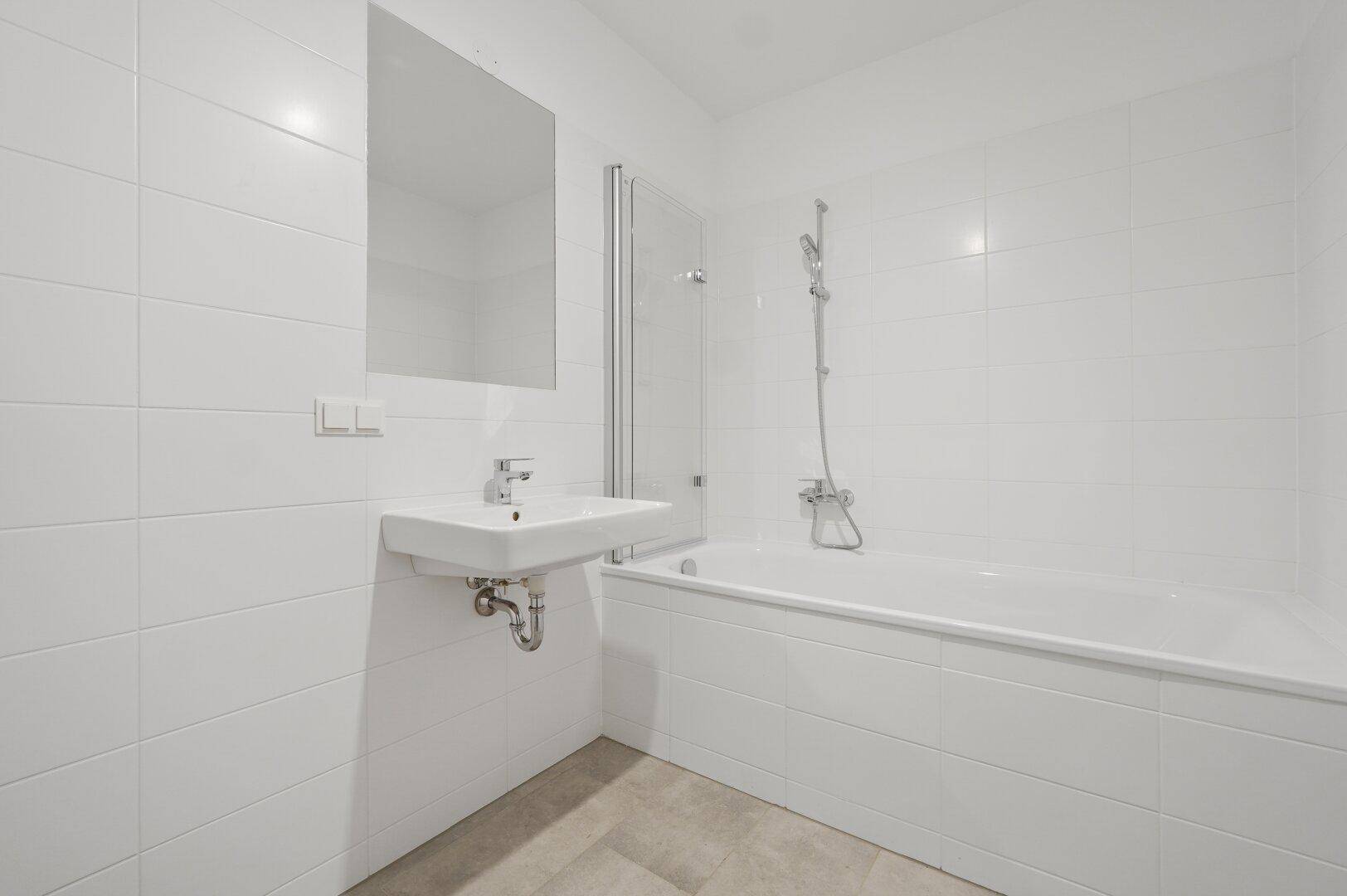Modernes Badezimmer mit Badewanne, Waschbecken und weißen Fliesen an den Wänden und am Boden.