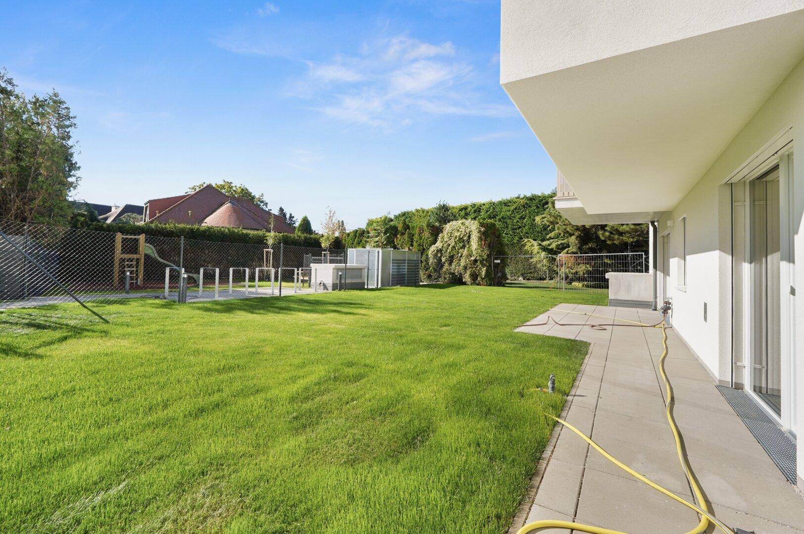 Großer Gemeinschaftsgarten mit Spielbereich und Zugang zu den Terrassen des modernen Gebäudes.