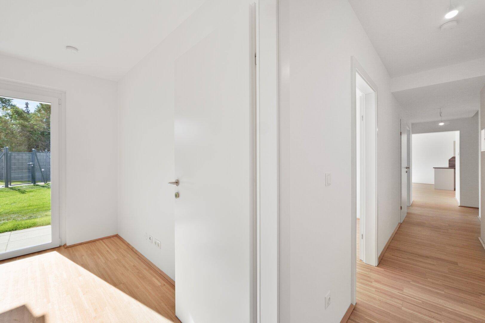 Heller Flur mit Holzboden, der zu verschiedenen Zimmern und zum Garten führt.
