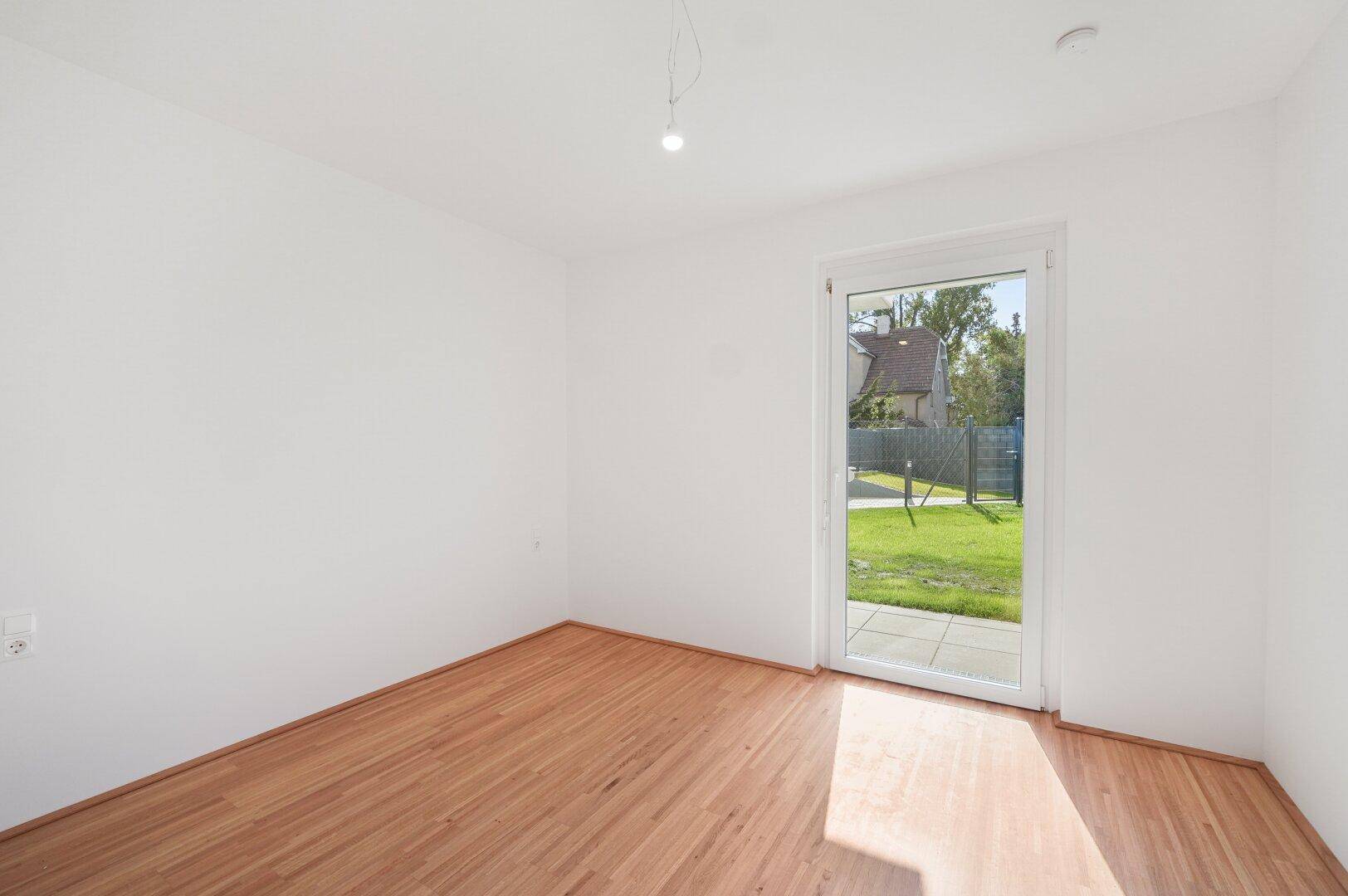 Helles Zimmer mit Holzboden und direktem Zugang zum Garten, ideal als Schlaf- oder Arbeitszimmer.
