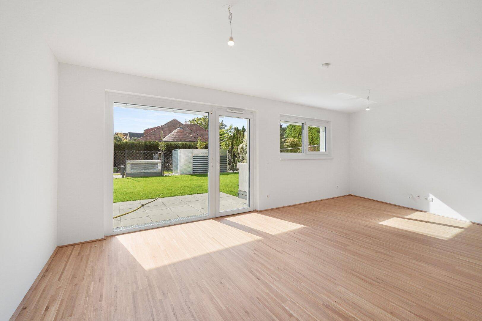 Großzügiger Raum mit Holzboden und breiter Fensterfront zum Garten, ideal für Wohnzwecke.