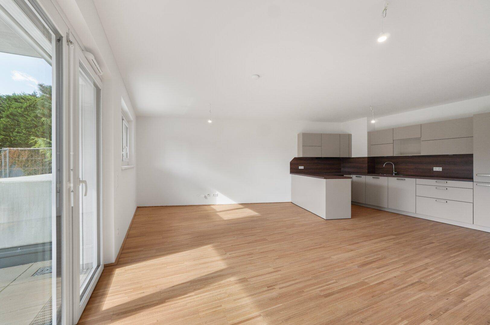 Heller, offener Wohnbereich mit integrierter Küche, Holzboden und Zugang zu einem Balkon.