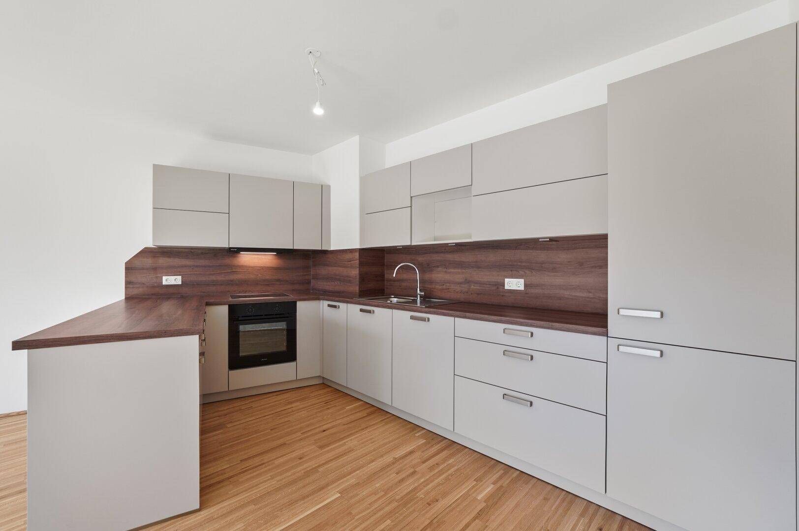 Moderne Einbauküche in Grau mit Holz-Arbeitsplatten und integriertem Backofen in einem hellen Raum.