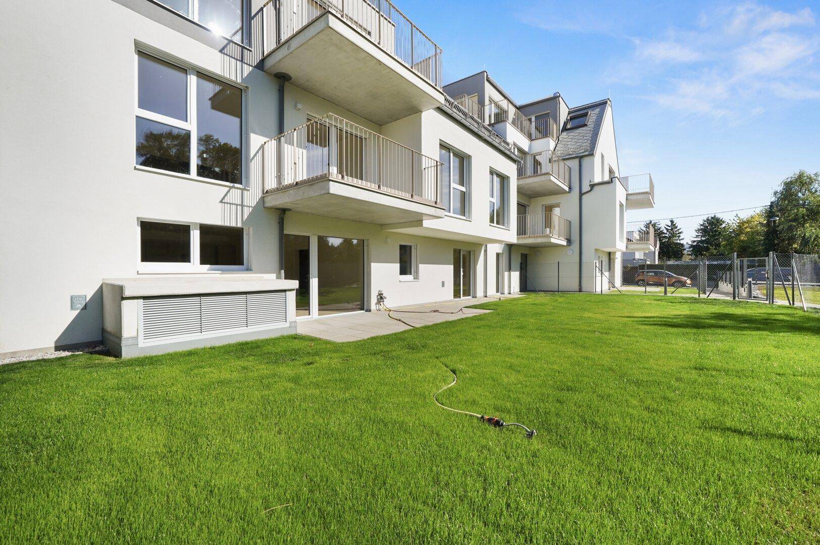 Weitläufiger Rasenbereich vor einem modernen Mehrfamilienhaus mit Balkonen und Terrassen.