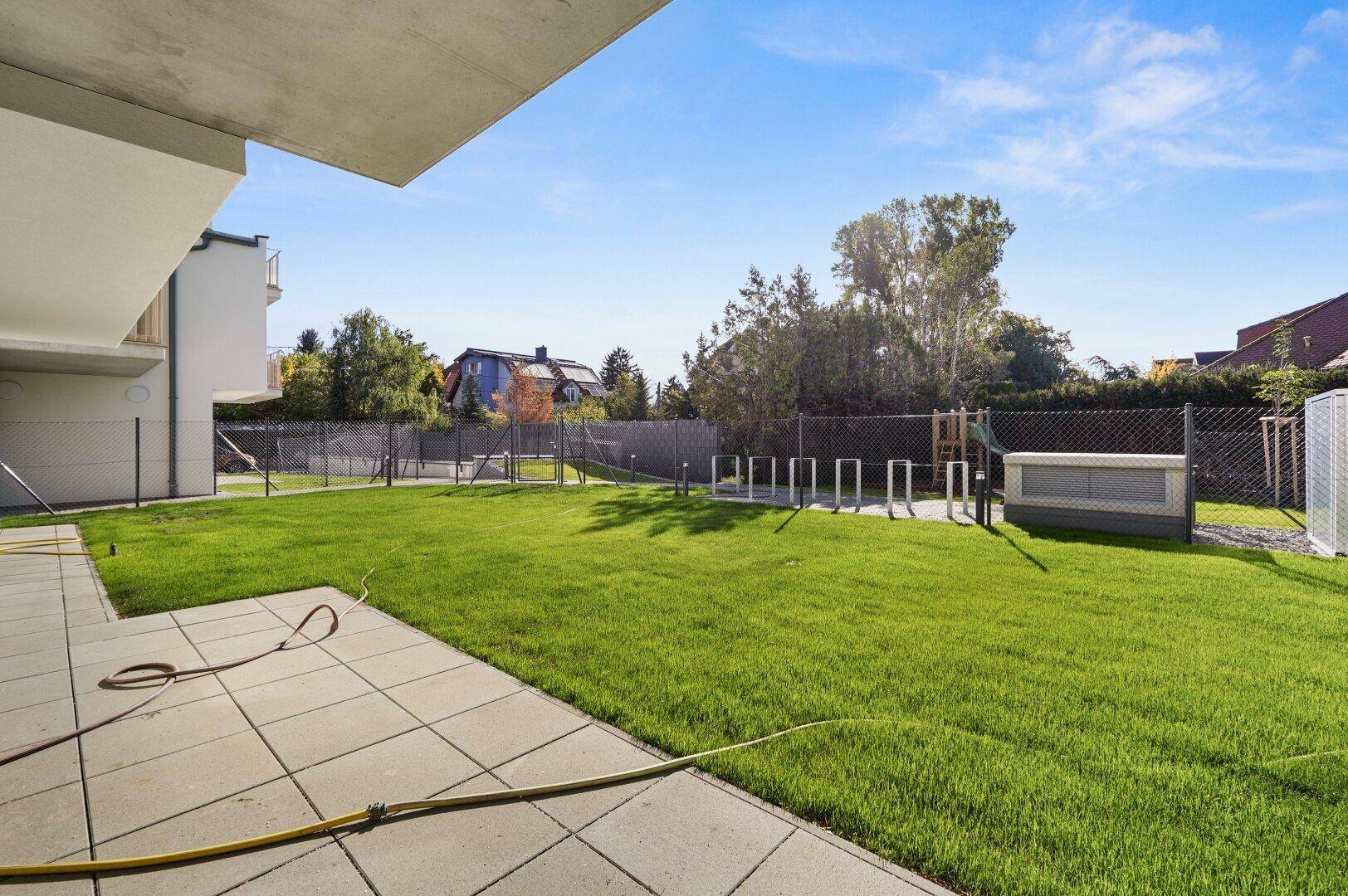 Gemeinschaftlicher Gartenbereich mit Spielplatz, Fahrradständern und gepflegtem Rasen.