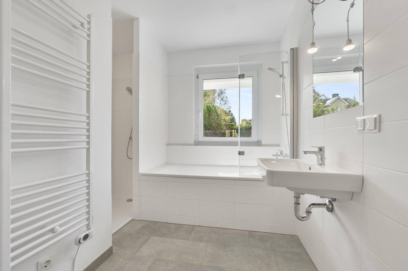 Modernes Badezimmer in Weiß mit Dusche, Badewanne, Waschbecken und beheiztem Handtuchhalter.