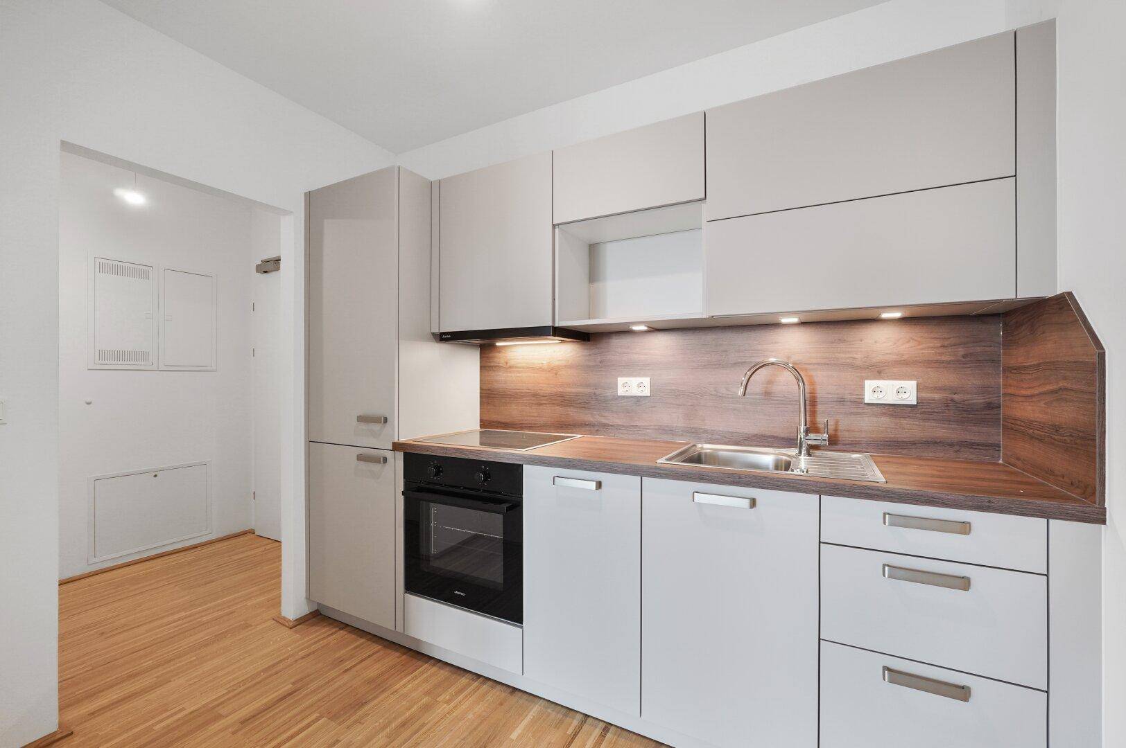 Moderne Einbauküche mit grauen Schränken, Holzarbeitsplatte und integrierten Geräten in hellem Design.