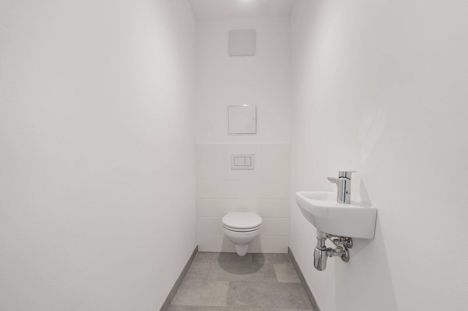 Separates Gäste-WC mit wandhängender Toilette und kleinem Waschbecken.
