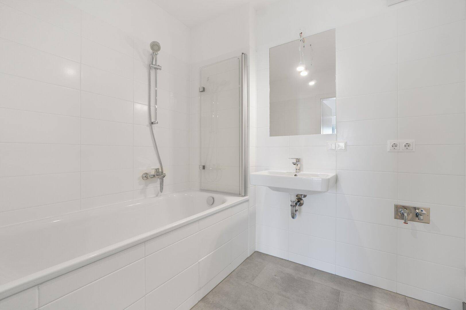 Modernes Badezimmer mit Badewanne, Duschabtrennung und weiß gefliesten Wänden.
