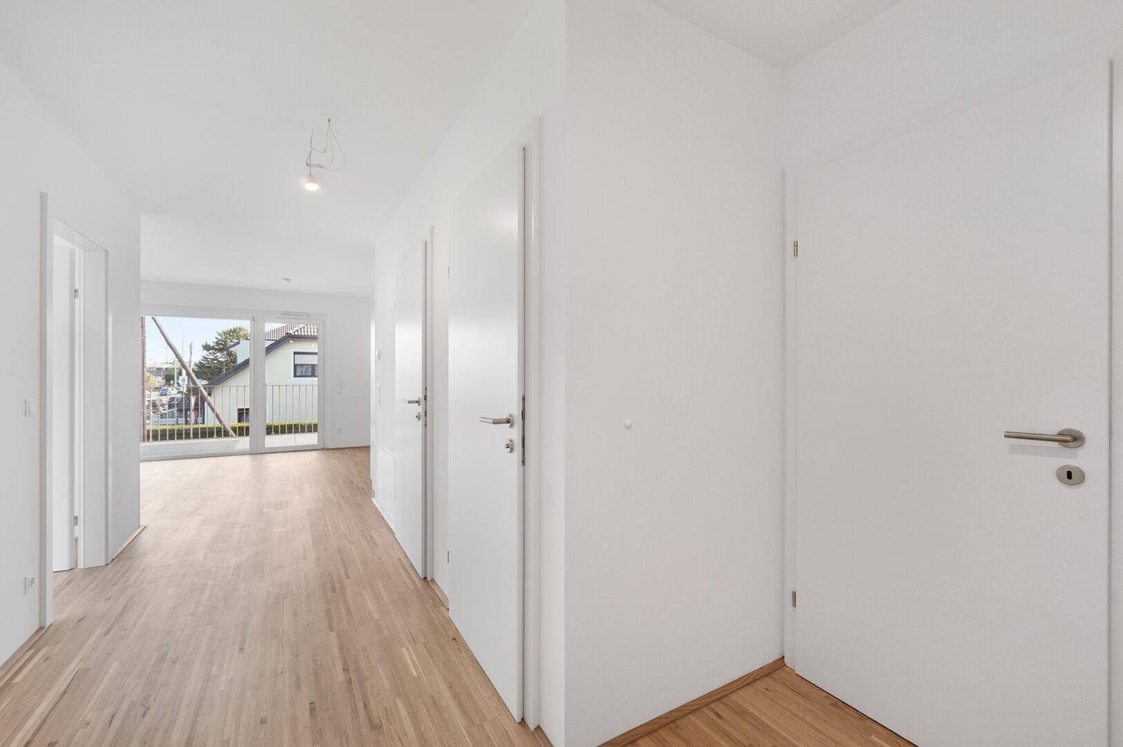 Heller Flur mit Holzboden und weißen Türen, der zum Wohnbereich und Balkon führt.