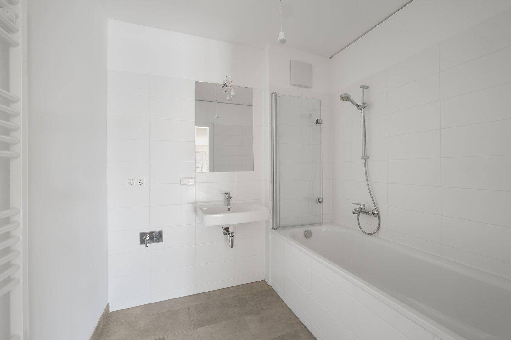 Modernes Badezimmer mit weißen Fliesen, Badewanne mit Duschwand und Handtuchheizkörper.