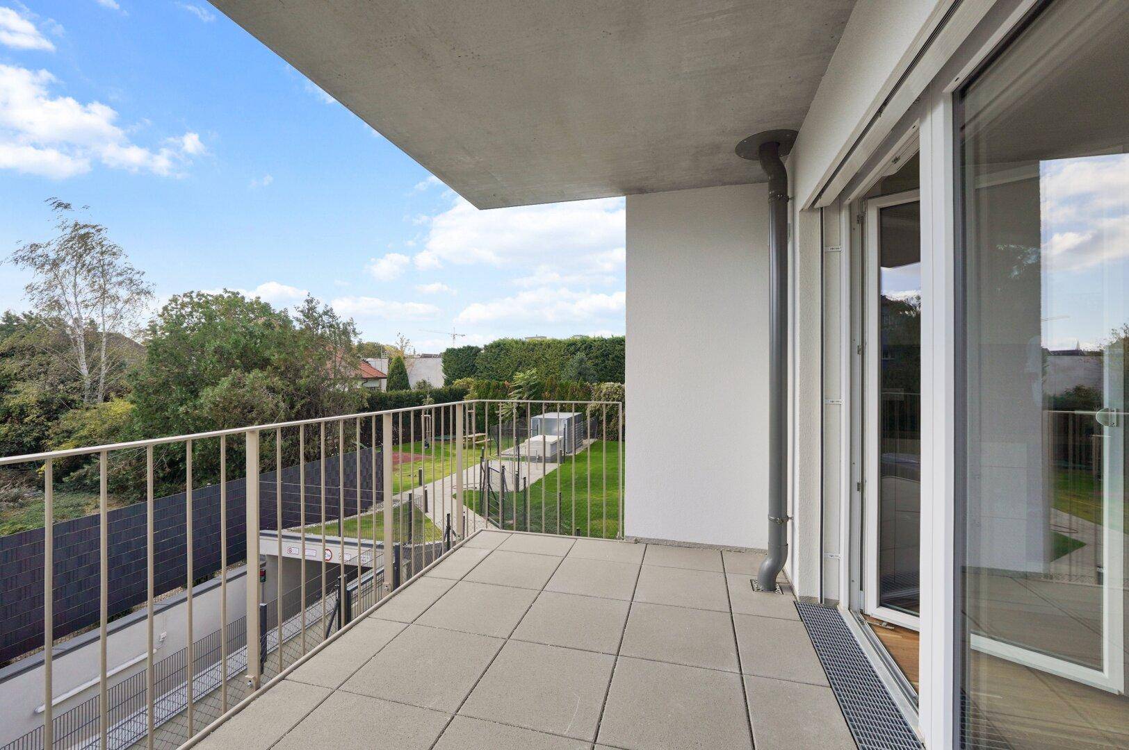 Heller Balkon mit Fliesenboden und Metallgeländer, bietet einen weiten Blick ins Grüne.