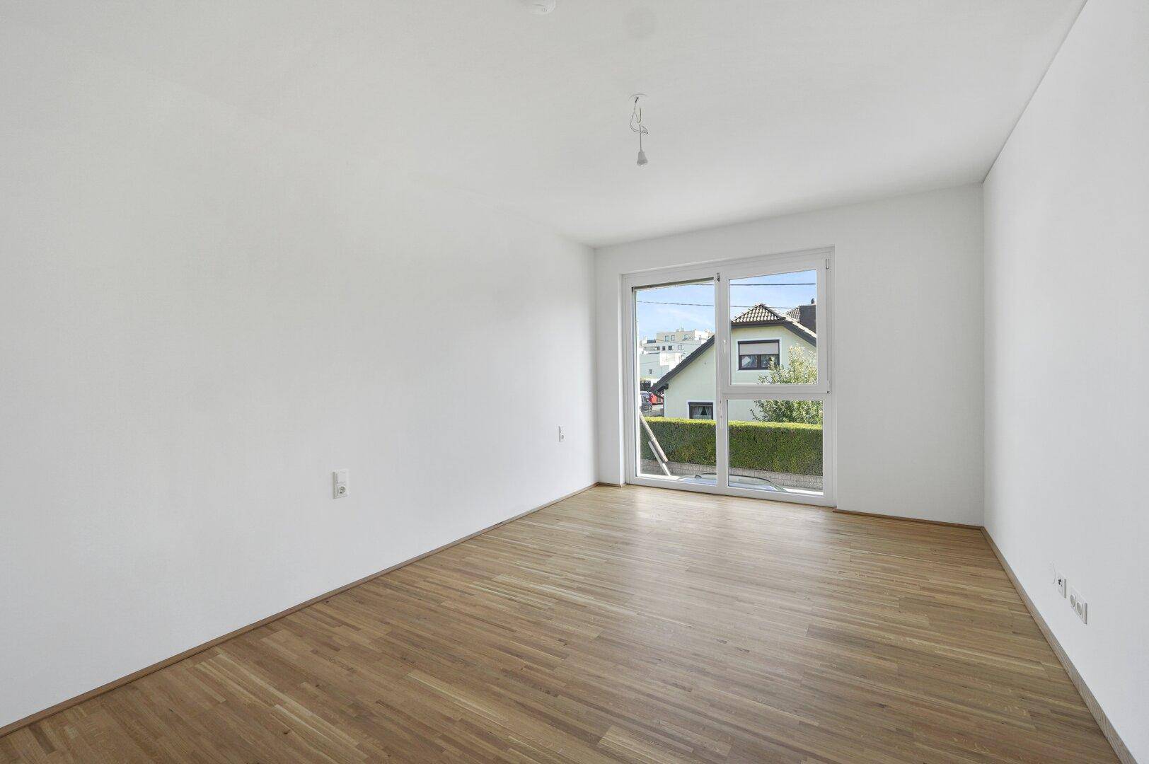 Geräumiges Zimmer mit hellem Parkettboden und viel Tageslicht durch das große Fenster.