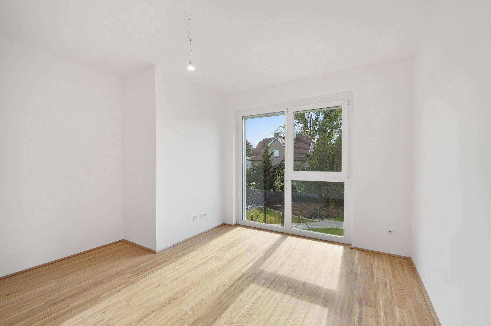 Helles Schlafzimmer mit Parkettboden und großem Fenster mit Blick ins Grüne.
