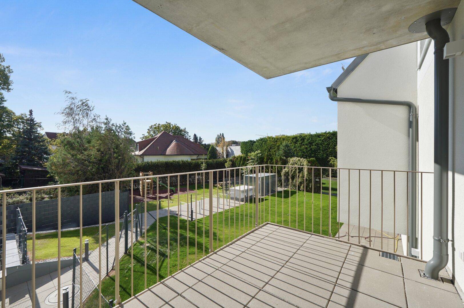 Geräumiger Balkon mit Fliesenboden und Blick auf den gepflegten Gemeinschaftsgarten.