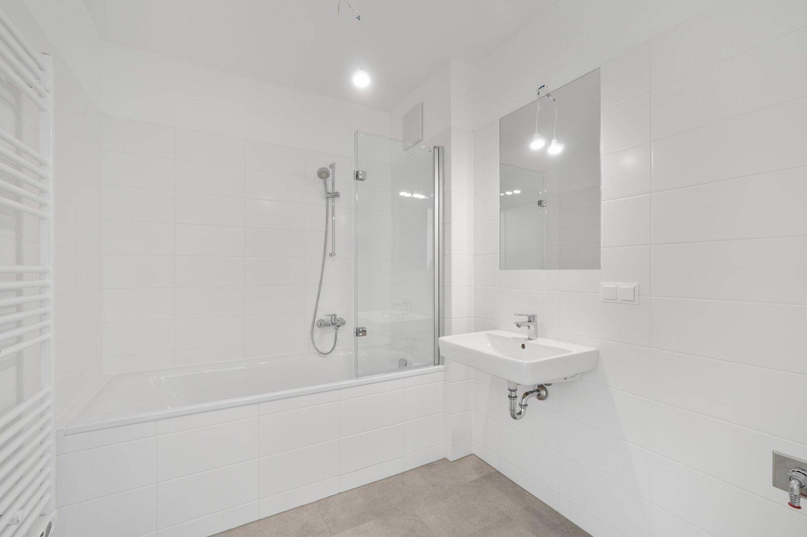 Modernes Badezimmer mit weiß gefliesten Wänden, Badewanne mit Duschabtrennung und Handtuchheizkörper.