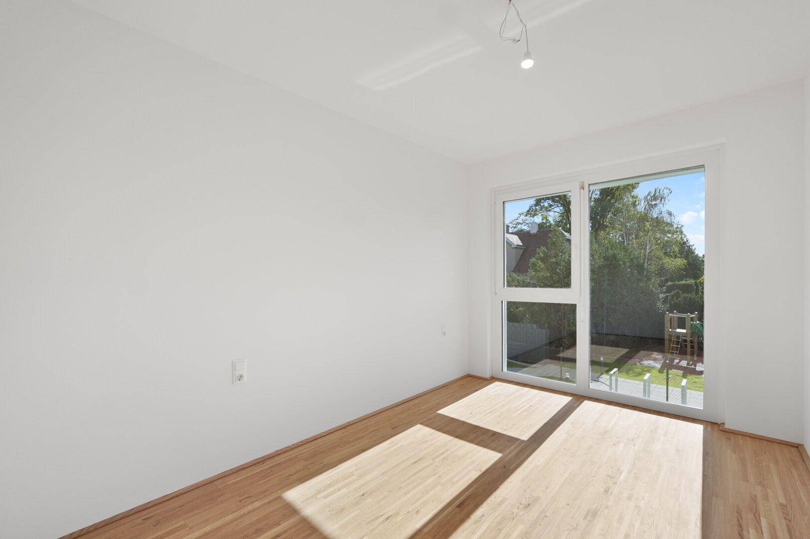 Helles Schlafzimmer mit Holzboden und großem Fenster mit Blick ins Grüne.