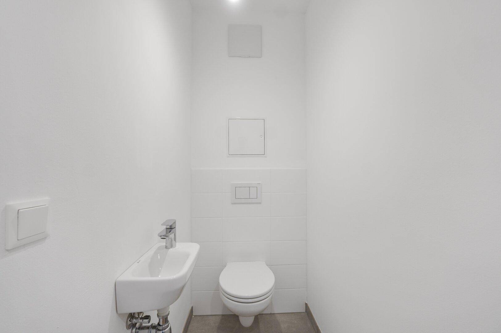 Separates Gäste-WC mit wandhängender Toilette und kleinem Handwaschbecken.