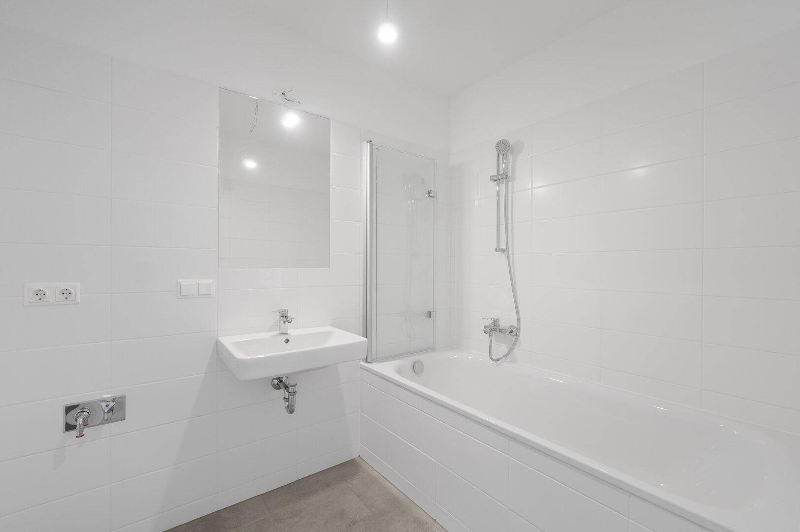 Helles Badezimmer mit Badewanne, Waschbecken und weißen Fliesen an den Wänden.
