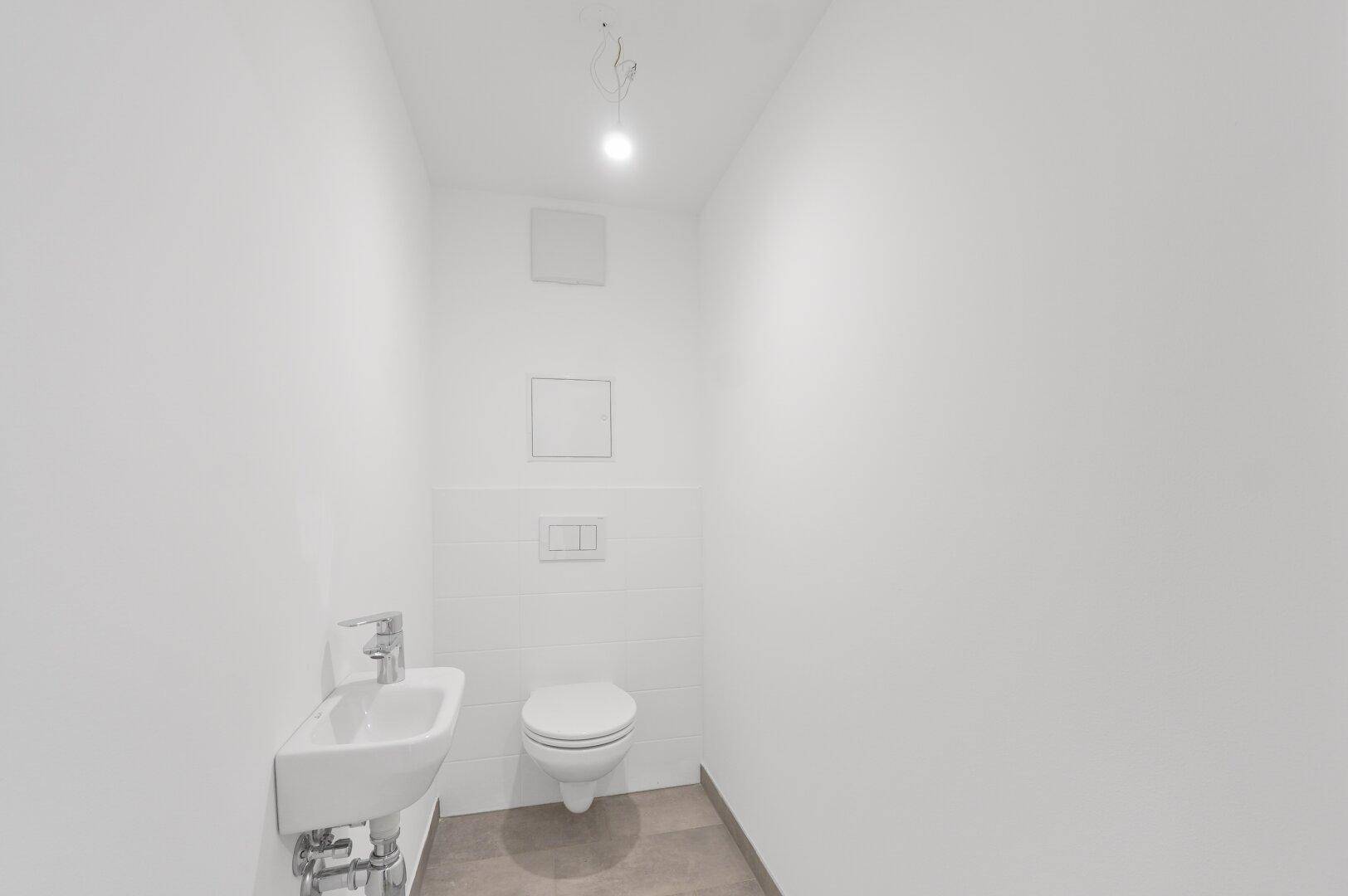 Separates Gäste-WC mit wandhängendem WC, kleinem Waschbecken und weißen Wandfliesen.
