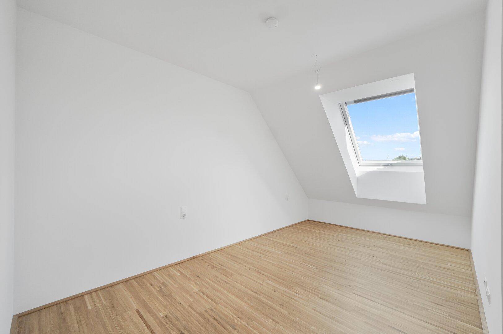 Leeres Zimmer im Dachgeschoss mit hellem Holzboden und einem Dachfenster für viel Tageslicht.