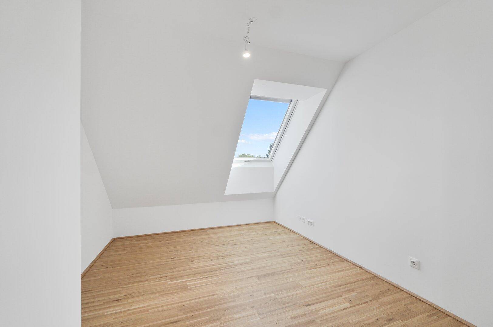 Helles, unmöbliertes Zimmer mit Holzboden und schrägem Dachfenster, ideal als Schlaf- oder Arbeitszimmer.