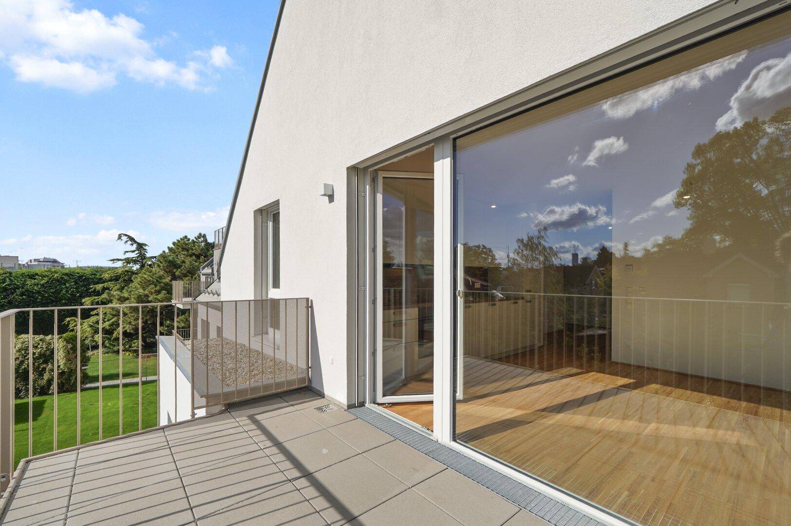 Geräumiger Balkon mit Fliesenboden und Metallgeländer, bietet einen weiten Blick ins Grüne.