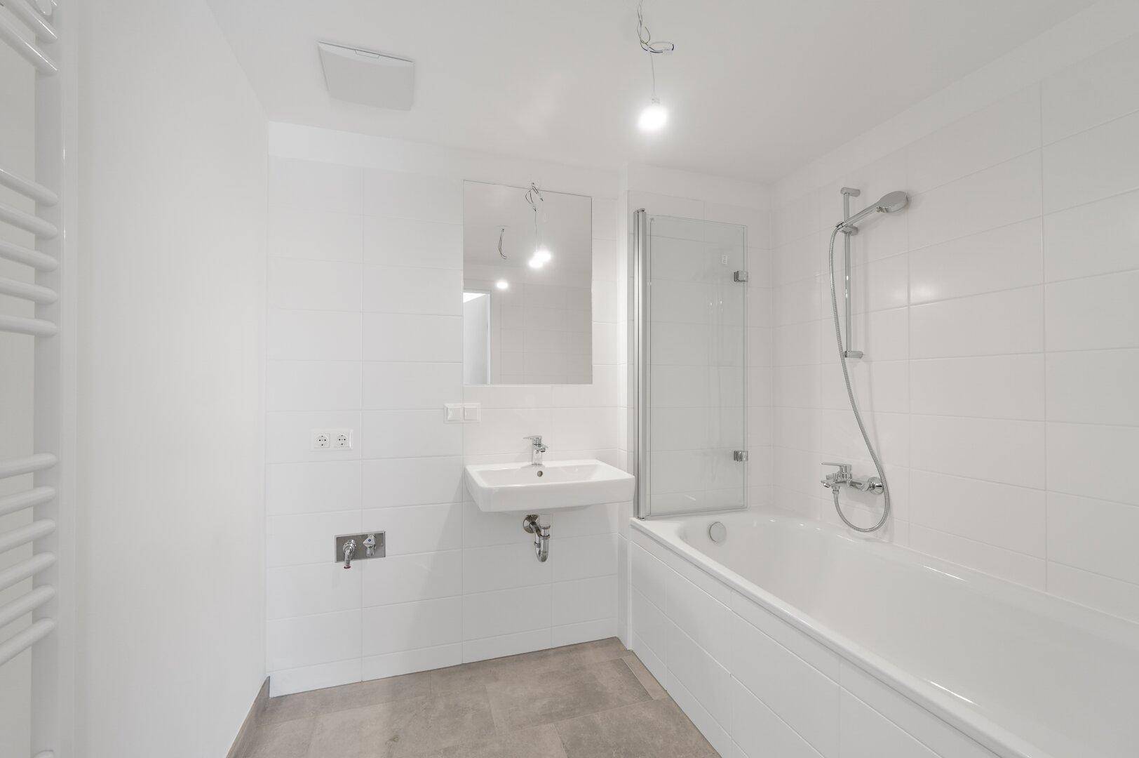Modernes Badezimmer mit Badewanne, Waschbecken, weißen Fliesen und beheiztem Handtuchhalter.