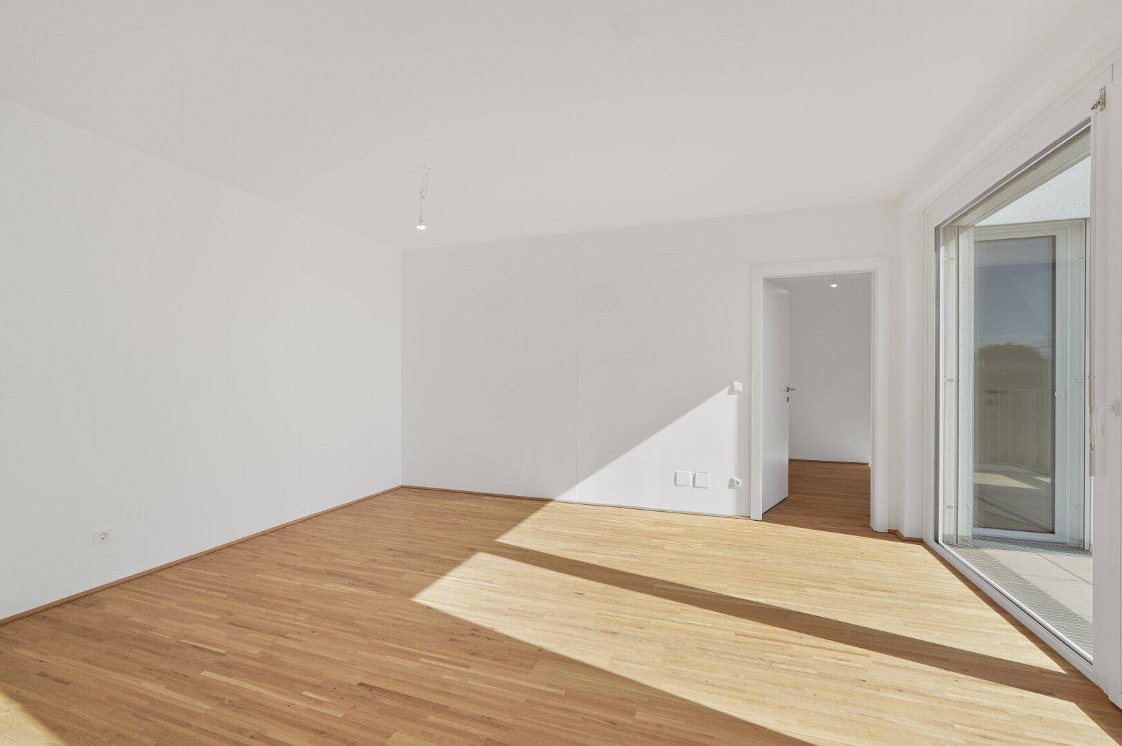 Geräumiges, helles Zimmer mit Holzboden und Zugang zu einem Außenbereich, perfekt als Wohnraum.