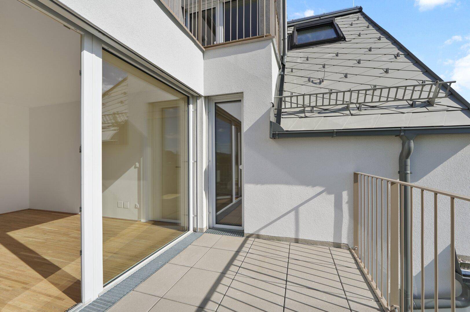 Heller Balkon mit Fliesenboden und Blick auf das Dach des Gebäudes und die Umgebung.
